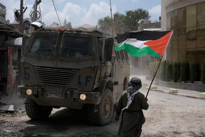 Cerita Tentang Warsiti, Nenek Penjual Kacang yang Menyumbang Rp 14 Seorang pria mengibarkan bendera Palestina saat kendaraan lapis baja Israel bergerak selama operasi militer di kamp Nur Shams, di Tepi Barat, Kamis, 29 Agustus 2024.
